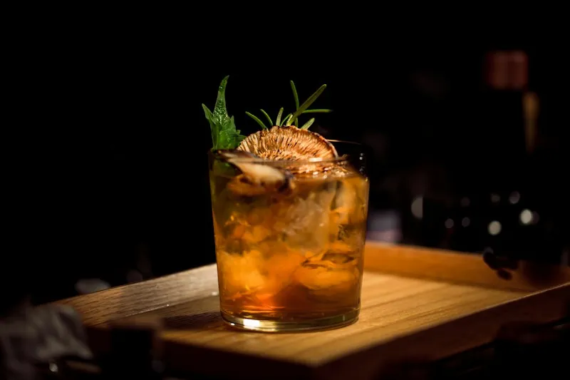 Cocktail with carved ice and citrus peel under warm bar light